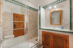 Ein Badezimmer mit Duschkabine aus Glas, Holzschrank, Waschbecken mit Spiegel und Toilette.