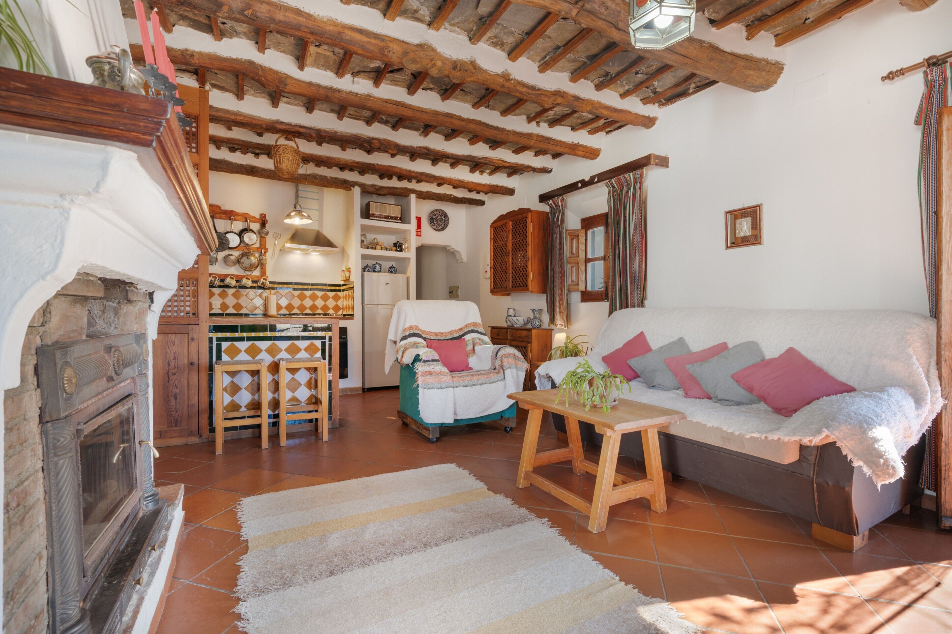 Una sala de estar acogedora con chimenea, un sofá, una mesa de madera y una zona de cocina con diversos objetos.
