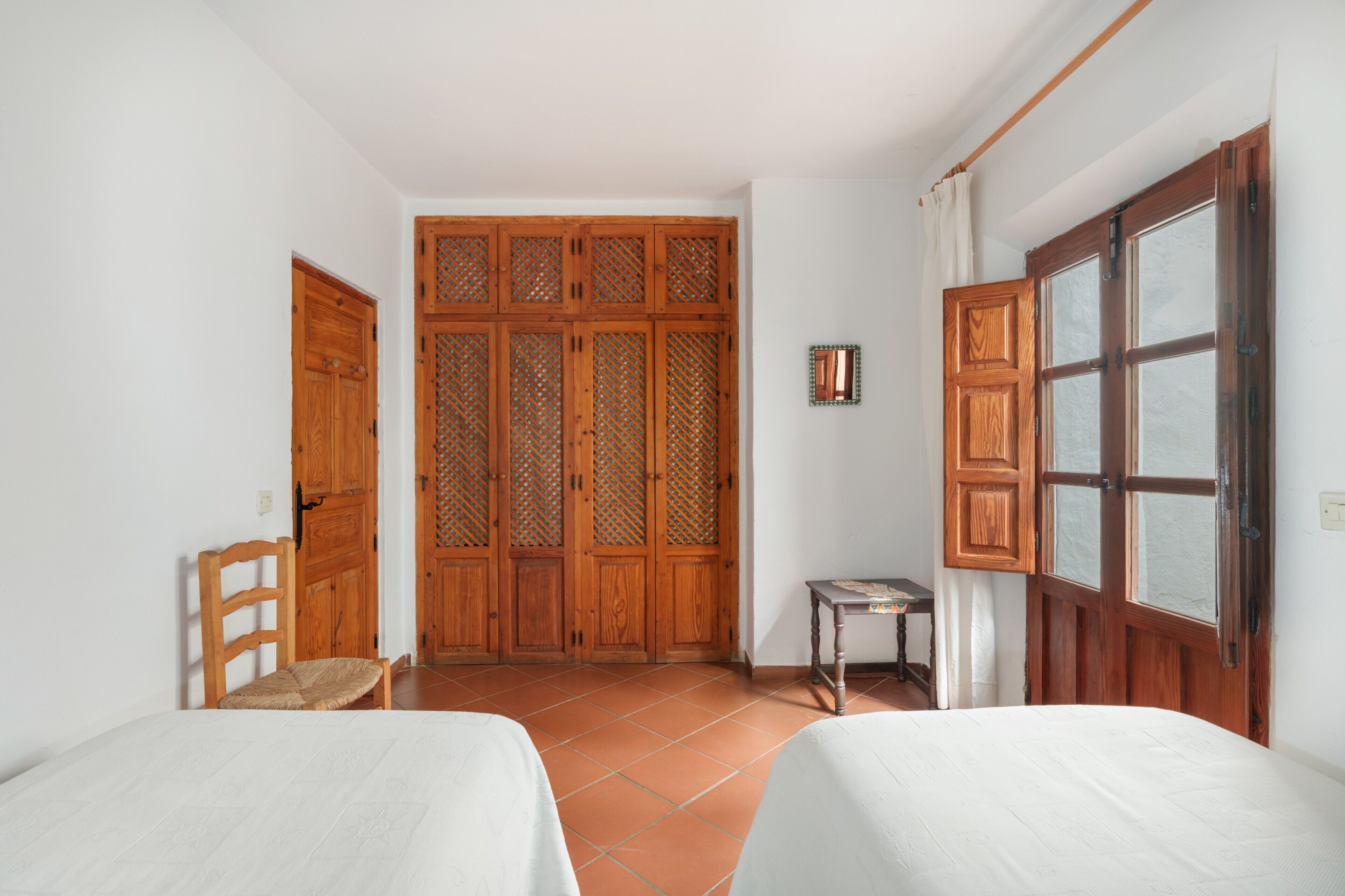 Una habitación con dos camas, un armario de madera, una mesita y una ventana.