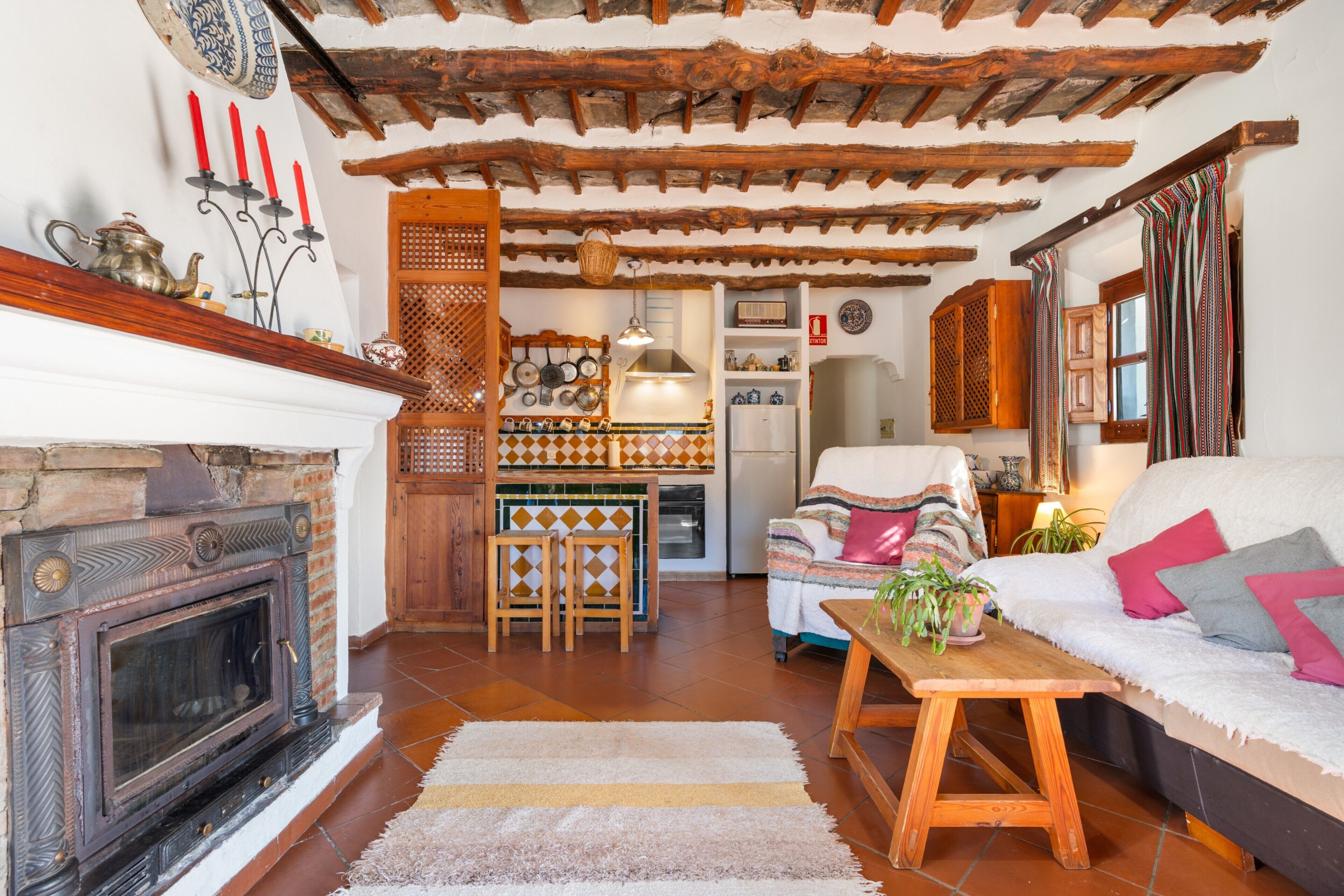 Una sala de estar rústica con chimenea, muebles de madera y una zona de cocina al fondo.