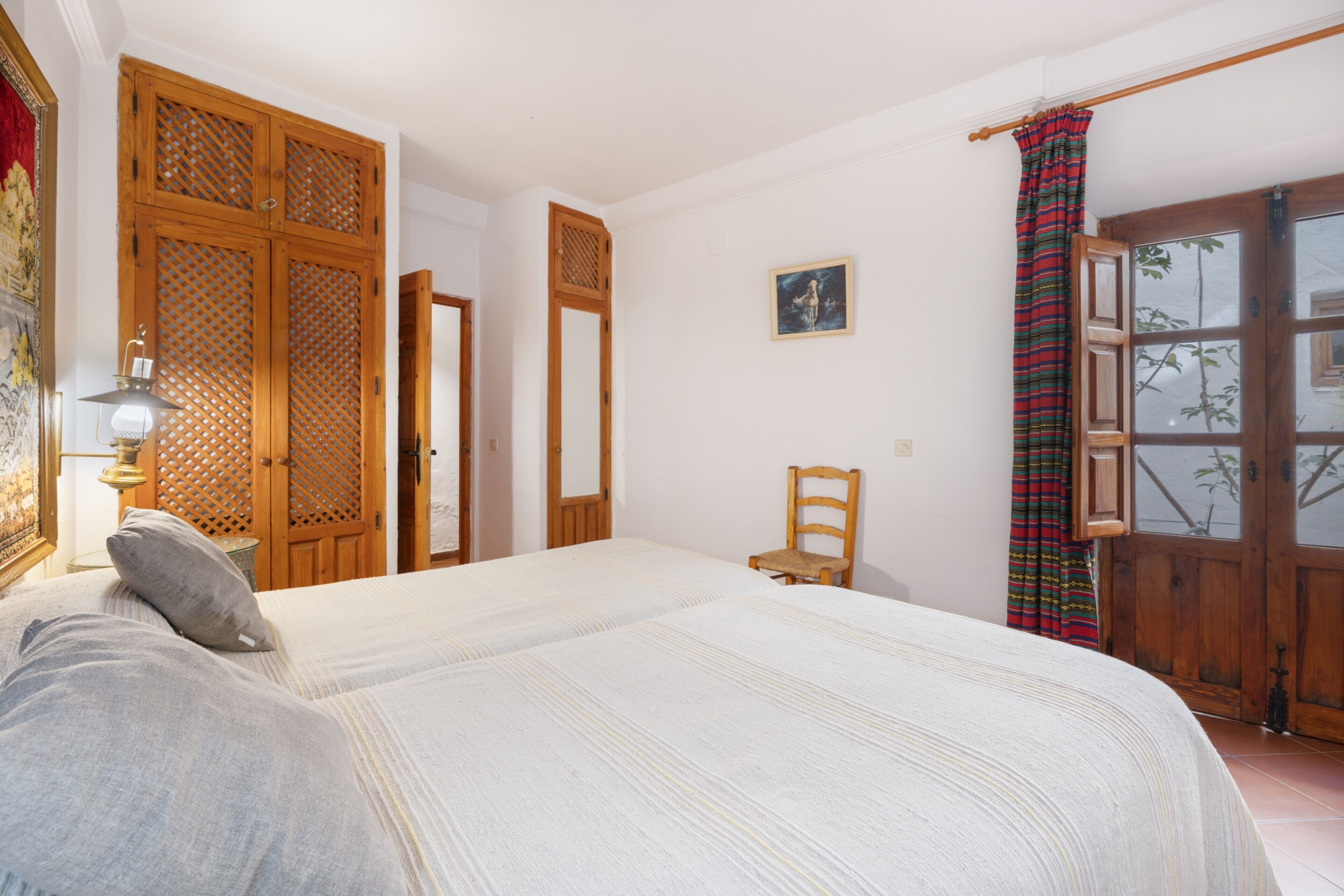 A bedroom with a large bed, wooden wardrobe, and a window with a view.
