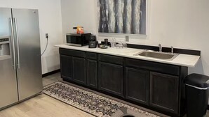 A modern kitchen with a stainless steel refrigerator, a microwave, a coffee maker, and a sink. - Food Truck Court BNB w/breakfast & pool table (Carlsbad)