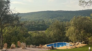 Un espace piscine doté d’une terrasse en bois, de chaises longues et offrant une vue sur une colline boisée.