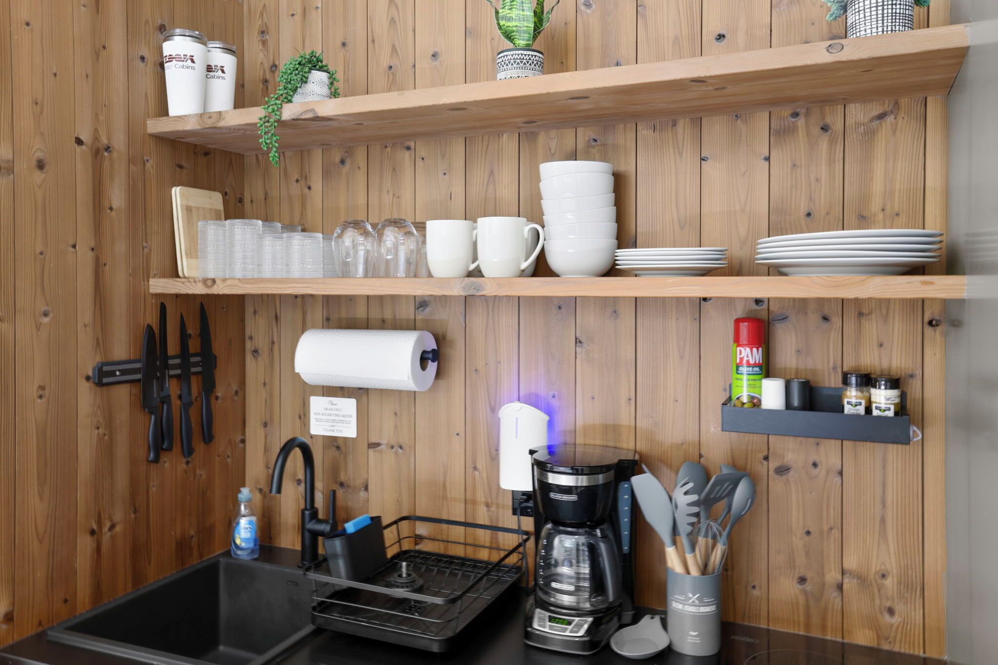 Cozinha com prateleiras de madeira contendo xícaras, pratos e uma cafeteira.