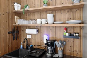 Et køkken med træhylder med kopper, tallerkener og en kaffemaskine.