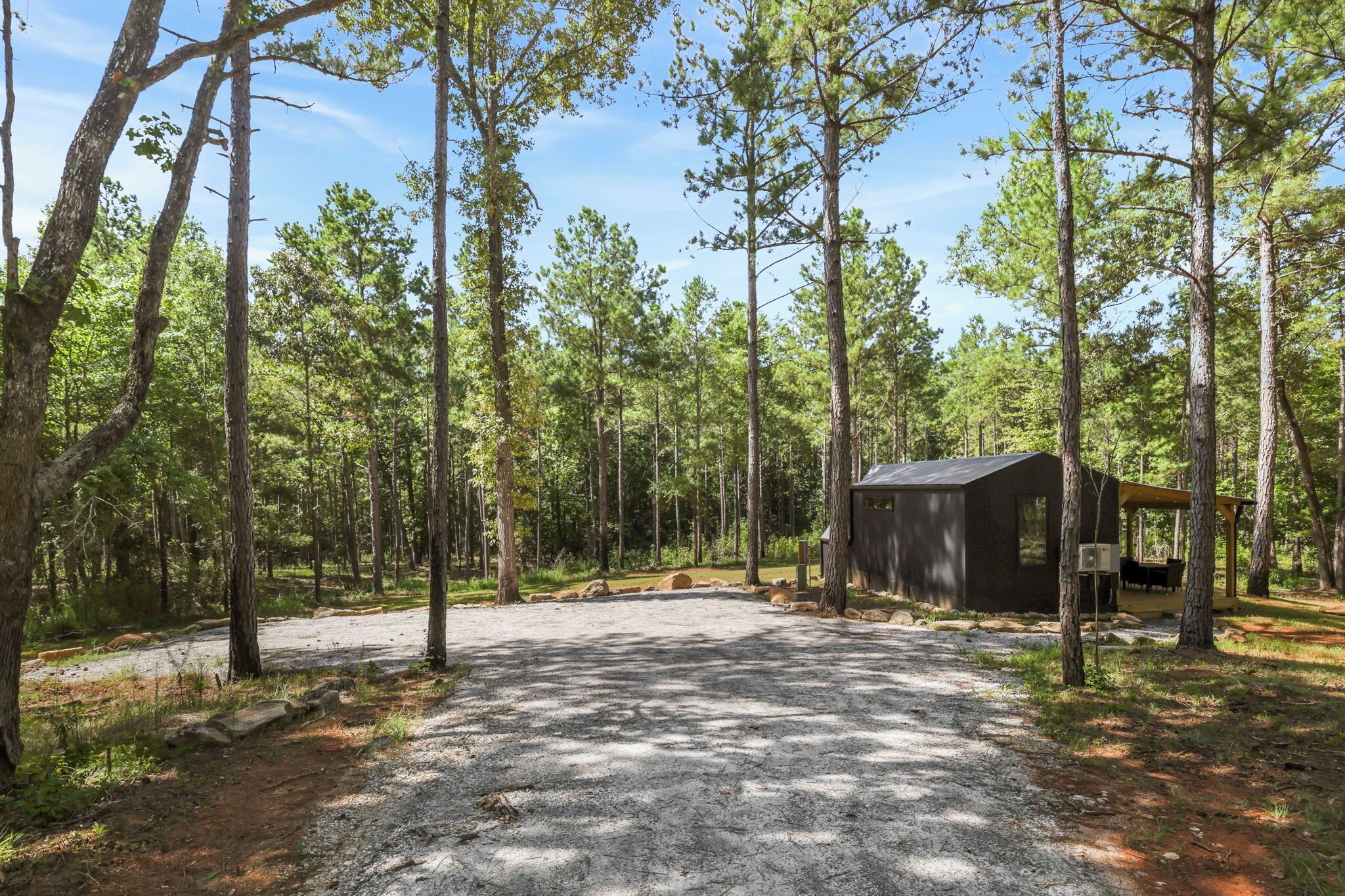 Um camping com área de estacionamento de cascalho, uma cabana pequena e uma mesa de piquenique.