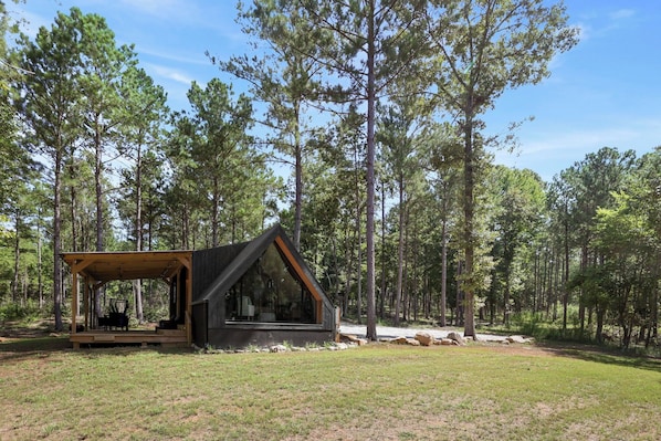 A cabin with a covered porch and a large window, surrounded by a forest. - Coldwater Cove - New Zook Cabin on 19 Acres (Elberton)