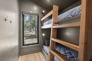 A compact room with bunk beds, a window with a forest view, and a door with a handle.