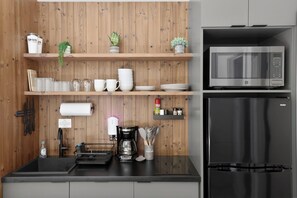 A modern kitchen with wooden shelves, a microwave, a refrigerator, and various kitchen utensils.
