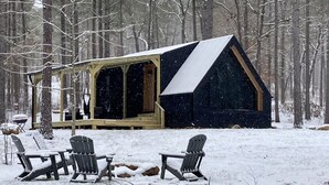 A cabin with a covered porch and two Adirondack chairs in a snowy forest.