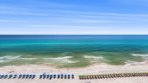 Ein Strand mit Reihen von Sonnenschirmen und Liegestühlen, ein sandiger Uferstreifen und der Ozean.