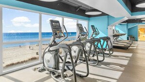 Ein Fitnessstudio mit Trainingsgeräten und großen Fenstern mit Blick auf einen Strand.