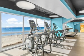 Ein Fitnessstudio mit Trainingsgeräten und großen Fenstern mit Blick auf einen Strand.
