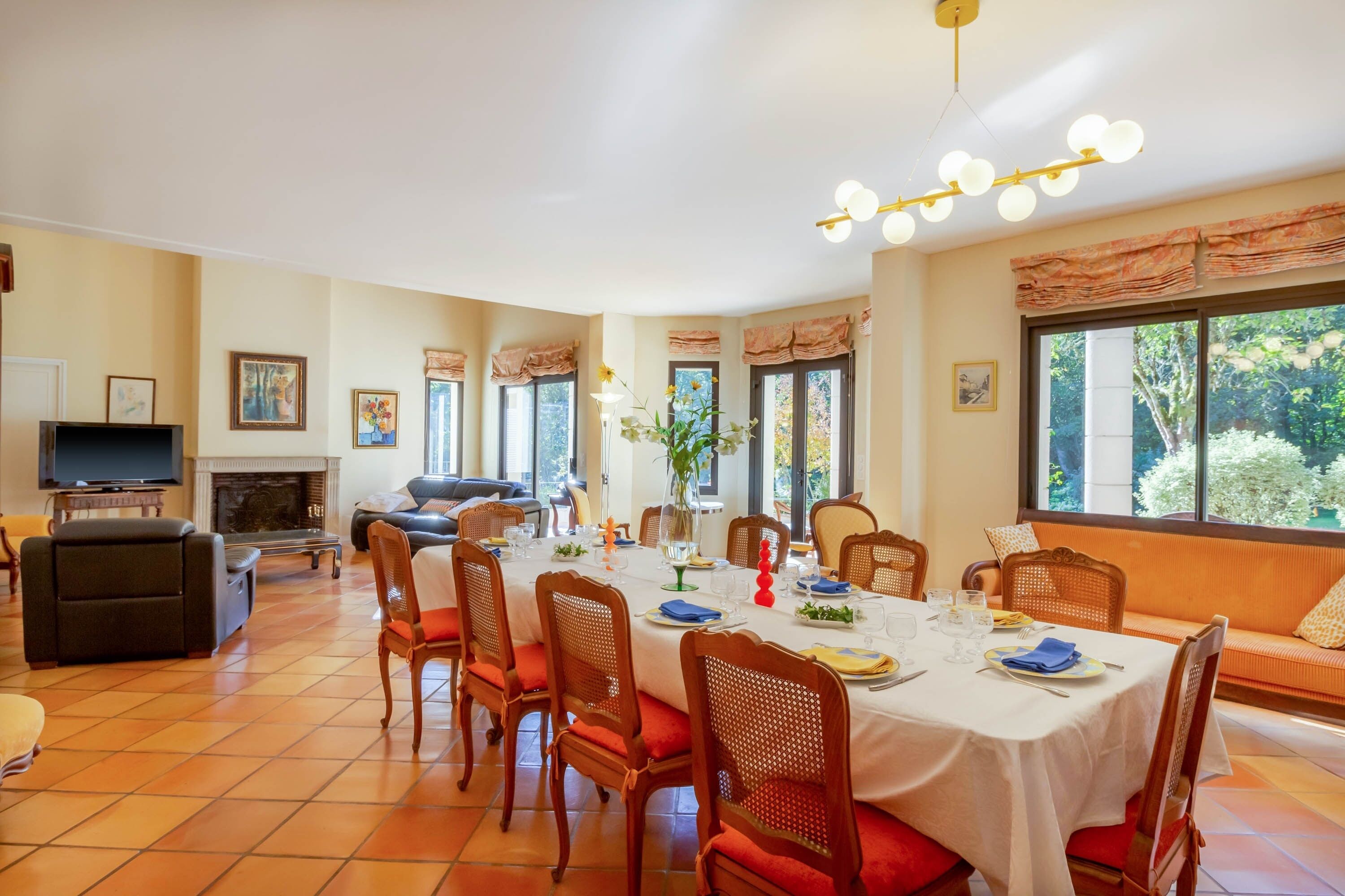 A dining area with a round table set for six, surrounded by wooden chairs with red cushions.