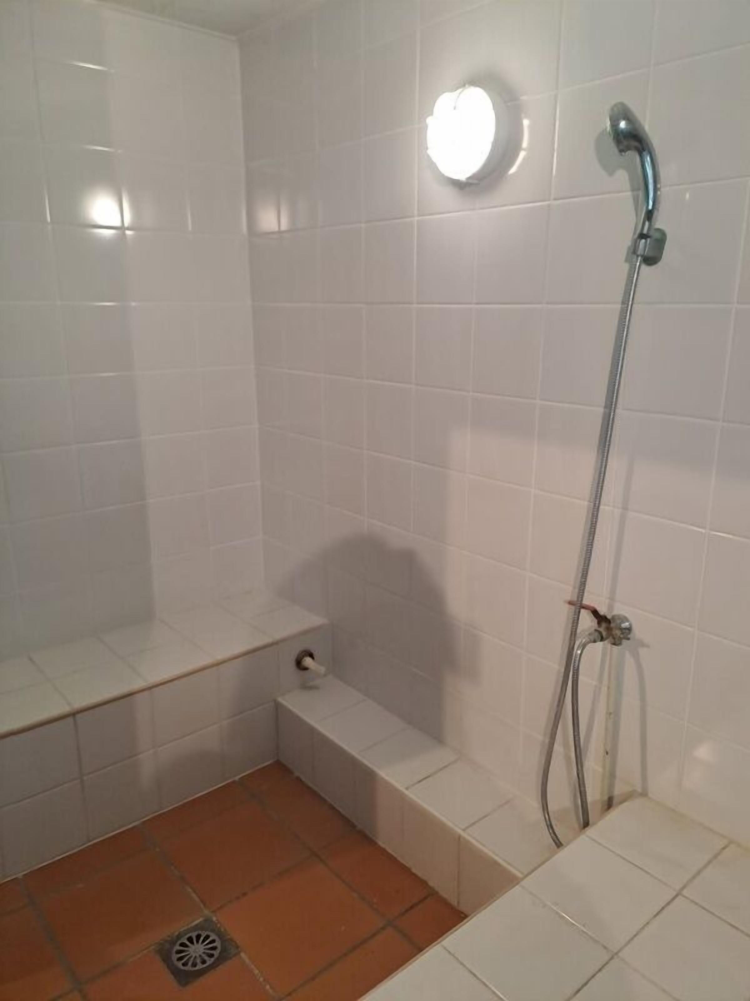 A small, tiled shower room with a handheld showerhead and a wall-mounted light.