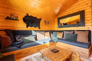 Ein gemütliches Blockhaus-Interieur mit Holzbalkendecke, einer Couch mit Kissen, einem Couchtisch, einem aufgehängten Schwarzbärenfell und einem Paar Ski.