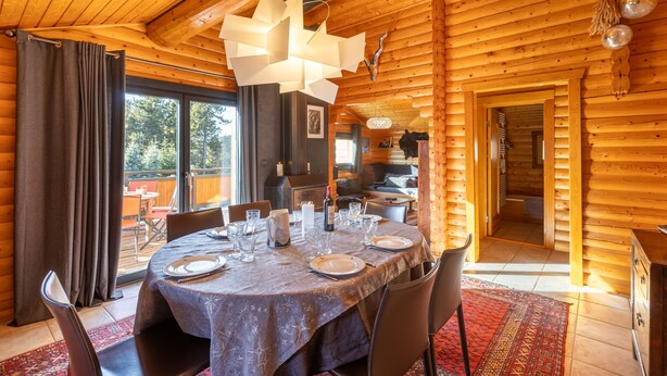 Ein Essbereich in einer Holzhütte mit einem runden Tisch, gedeckt für vier Personen, einer Kandelaber und Blick ins Freie.
