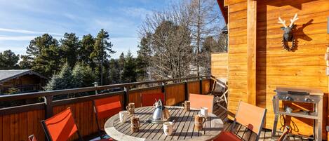 A wooden deck with a round table and chairs, a kettle, mugs, and a grill.