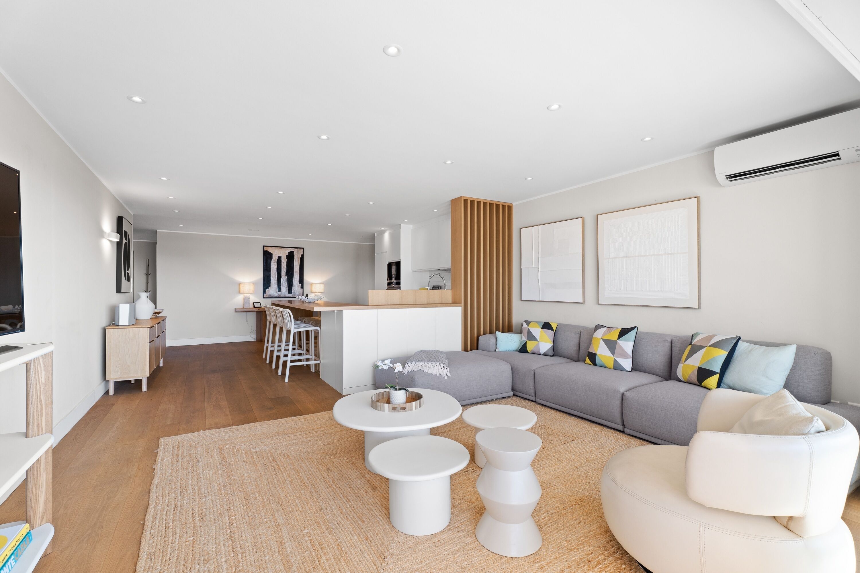 A modern living room with a sofa, coffee table, and chairs, a kitchen area, and a dining space.