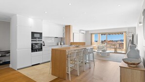 Een moderne keuken met witte kastjes, een houten kookeiland en barstoelen.