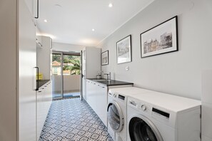A modern laundry room with a washing machine, a sink, and a glass door leading to a balcony. - Beaulieu Palace - Rooftop Vue Mer (Beaulieu-sur-Mer)