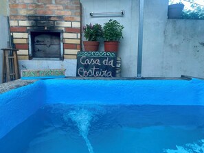 A pool with a blue edge, a brick fireplace, and a sign that reads 'Casa da Costeira.'