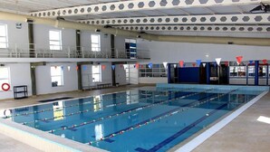 A large indoor swimming pool with multiple lanes, a spectator area, and a covered upper deck.