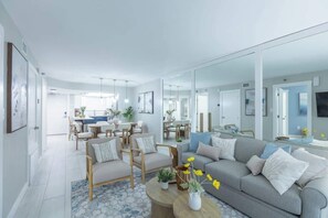 Ein modernes Wohnzimmer mit grauem Sofa, Holzstühlen, einem Couchtisch mit Blumenvase und einem großen Spiegel, der den Raum widerspiegelt.