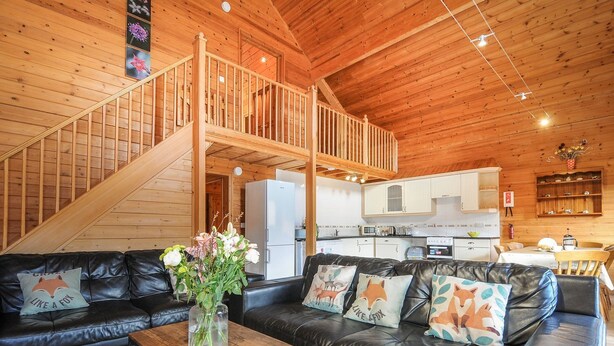 Un accogliente interno di una baita con una scala in legno, un soggiorno con divani in pelle, una zona pranzo e una cucina.