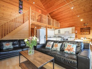 Un acogedor interior de cabaña con una escalera de madera, una sala de estar con sofás de cuero, un comedor y una cocina.