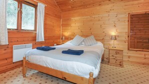 Camera da letto in una baita di legno con un letto, due comodini, una finestra con tende e un termosifone a parete.