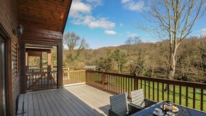 Un terrazzo in legno con posti a sedere all'aperto e una vista panoramica su alberi e colline.
