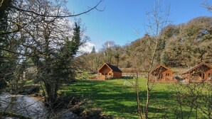 Una baita rustica con facciata in legno, immersa in un prato verde e rigoglioso, con un ruscello sullo sfondo.