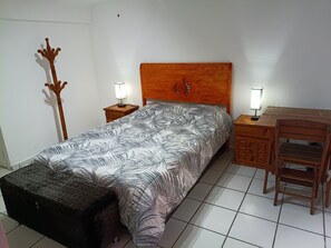 A bedroom with a bed, two bedside tables, a wooden headboard, a nightstand, a desk, and a chair.