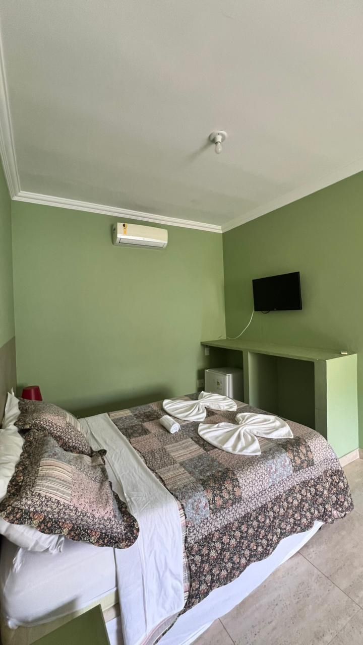 A hotel room with a bed, a flat-screen TV mounted on the wall, and a small desk with a chair.