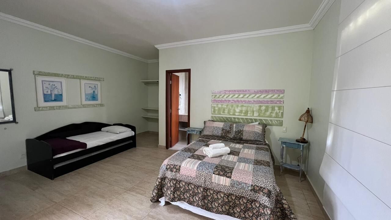 Quarto com cama, sofá-cama, mesa de cabeceira e prateleira na parede.
