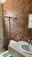 Un baño moderno con pared de madera, cabina de ducha de cristal, inodoro blanco y lavabo con espejo.