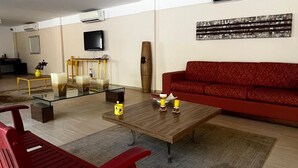 Un salon spacieux avec un canapé rouge, une table basse en verre et un banc rouge. Un téléviseur est fixé au mur et une sculpture en bois est posée sur le sol.