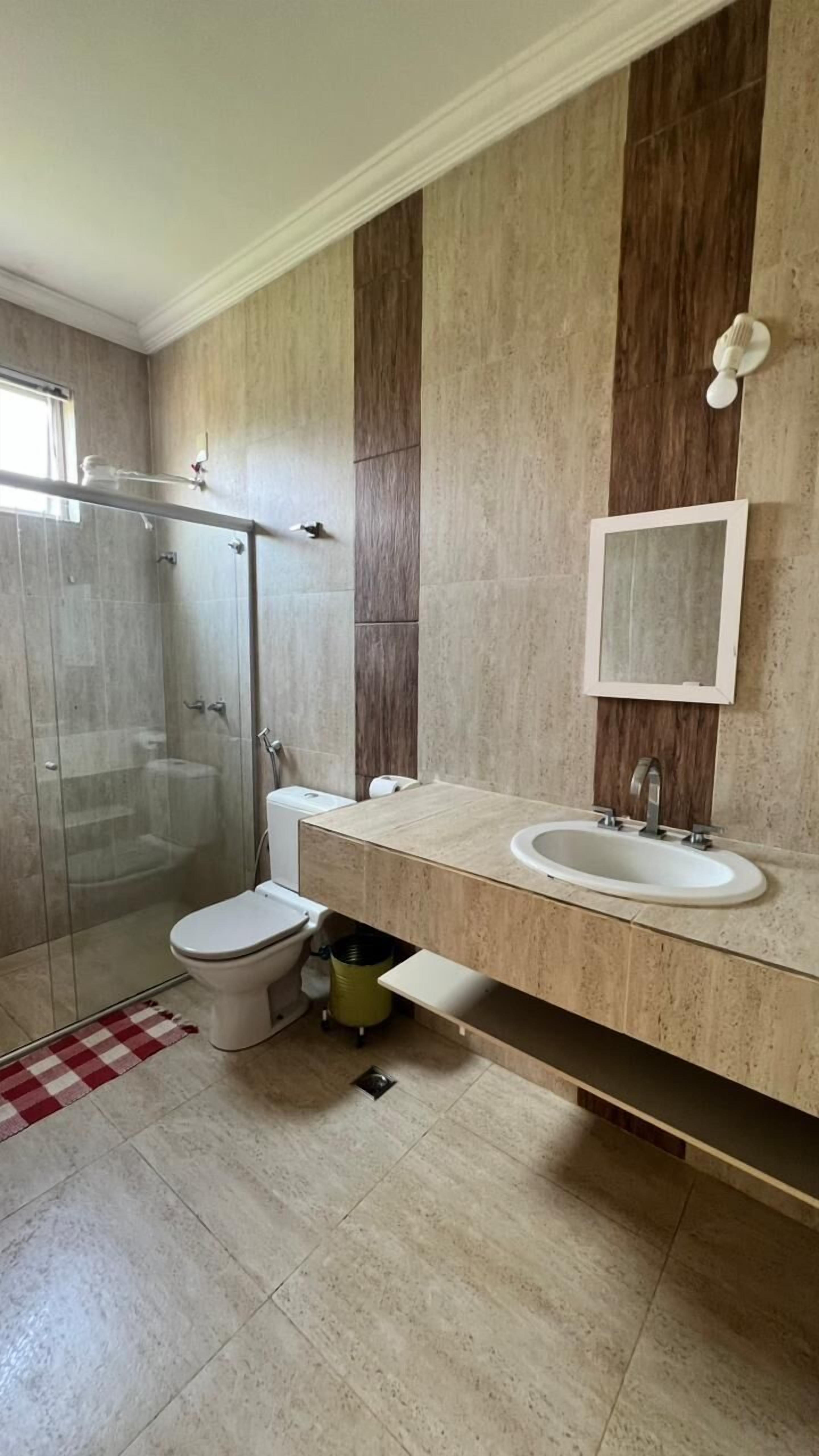 Uma casa de banho moderna com cabine de duche em vidro, sanita, lavatório e espelho.