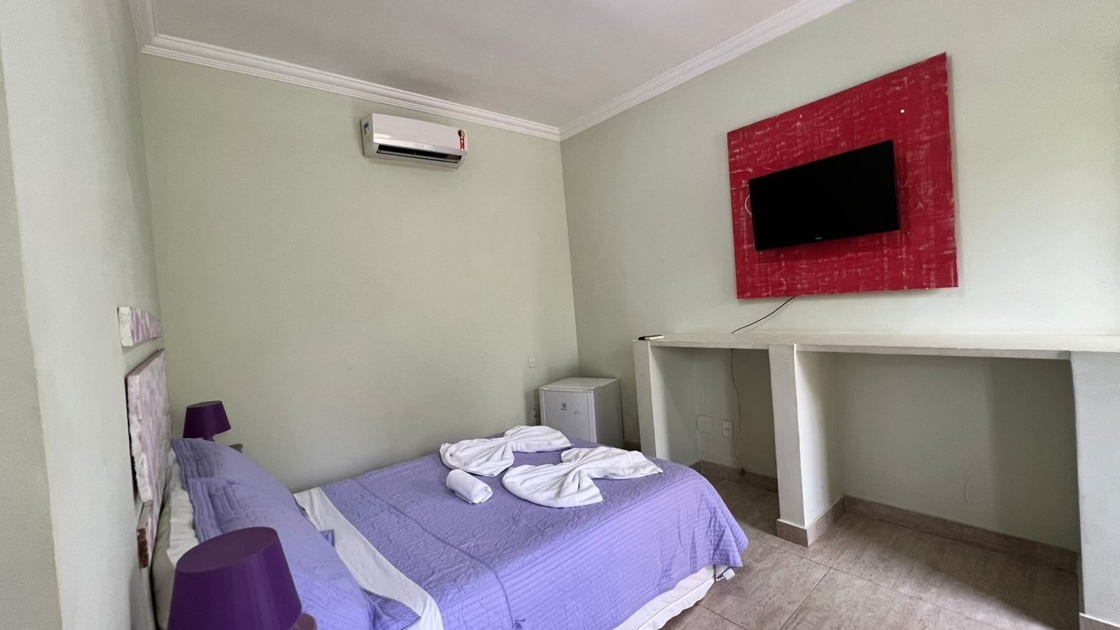 Een slaapkamer met een bed, een airconditioning, een bureau en een televisie aan de muur.