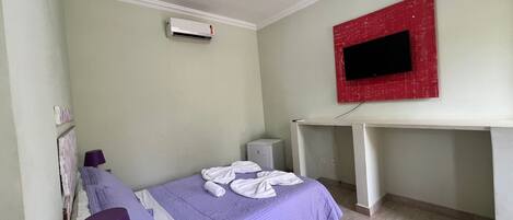 Een slaapkamer met een bed, een airconditioning, een bureau en een televisie aan de muur.