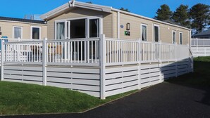 A mobile home with a fenced deck, a small porch, and a window with a curtain. - Caravan C31 at Landscove Holiday Park (Brixham)