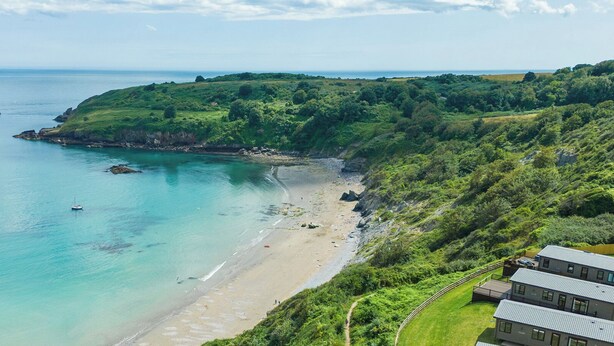 A coastal landscape with a sandy beach, a clear blue sea, and a grassy hill with buildings in the foreground. - Caravan C31 at Landscove Holiday Park (Brixham)