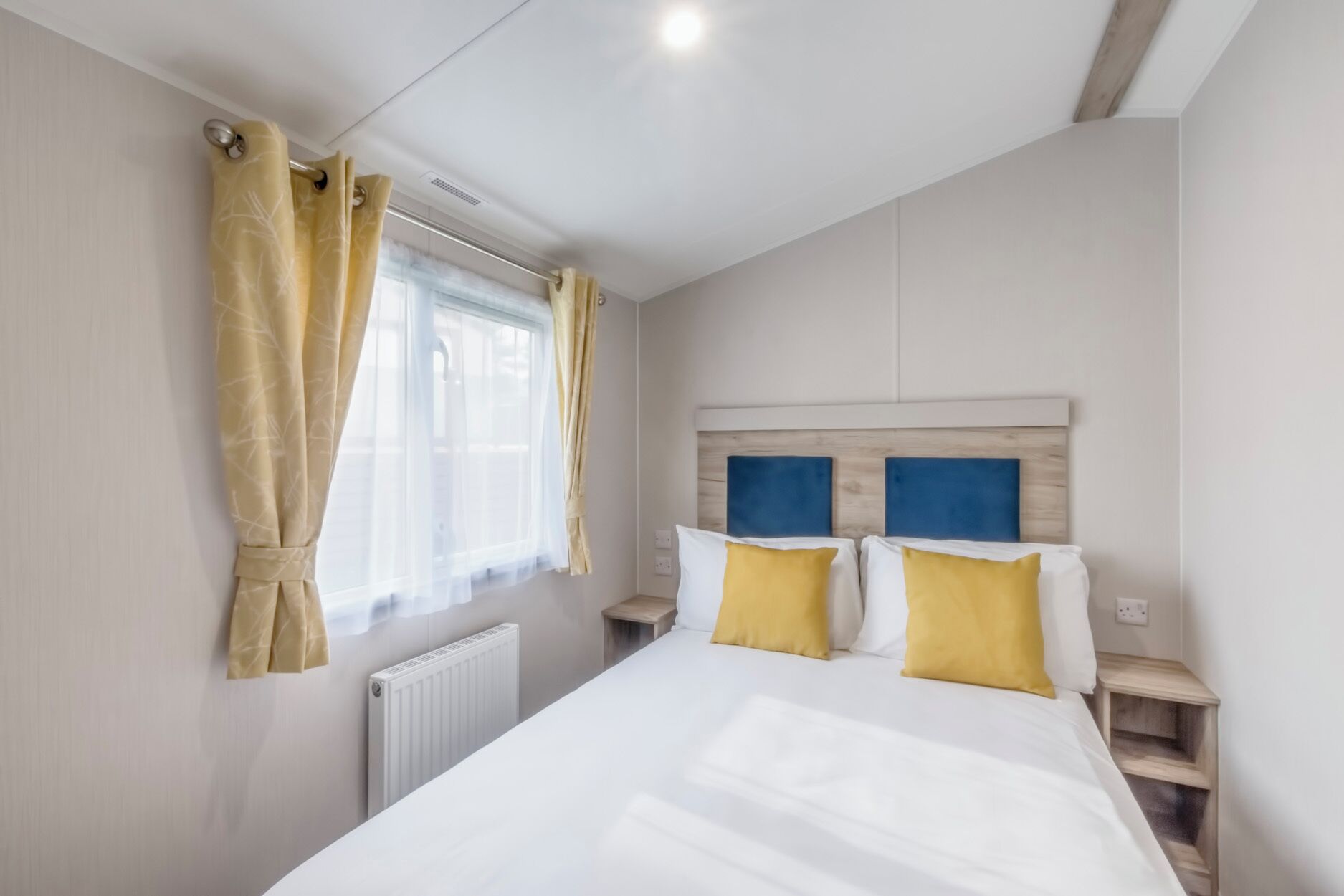 Ein Schlafzimmer mit einem Bett, zwei Nachttischen, einem Fenster mit Vorhängen und einer Heizung.