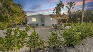 A house with a patio, a dining table, and a lounge area with a canopy. - The Pink House - Walking Distance to the Beach and Restaurants (Holmes Beach)