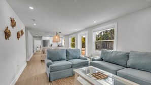 A modern living room with a sofa, a coffee table, and a kitchen in the background. - The Pink House - Walking Distance to the Beach and Restaurants (Holmes Beach)
