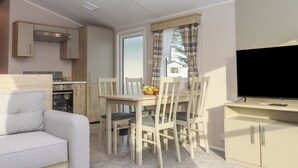 A compact living space with a dining area, kitchenette, and a TV. - Caravan B61 at Landscove Holiday Park (Brixham)