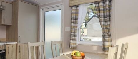 Eine kompakte Küche mit Holzschränken, einem Esstisch mit Stühlen und einem Fenster mit karierten Vorhängen.