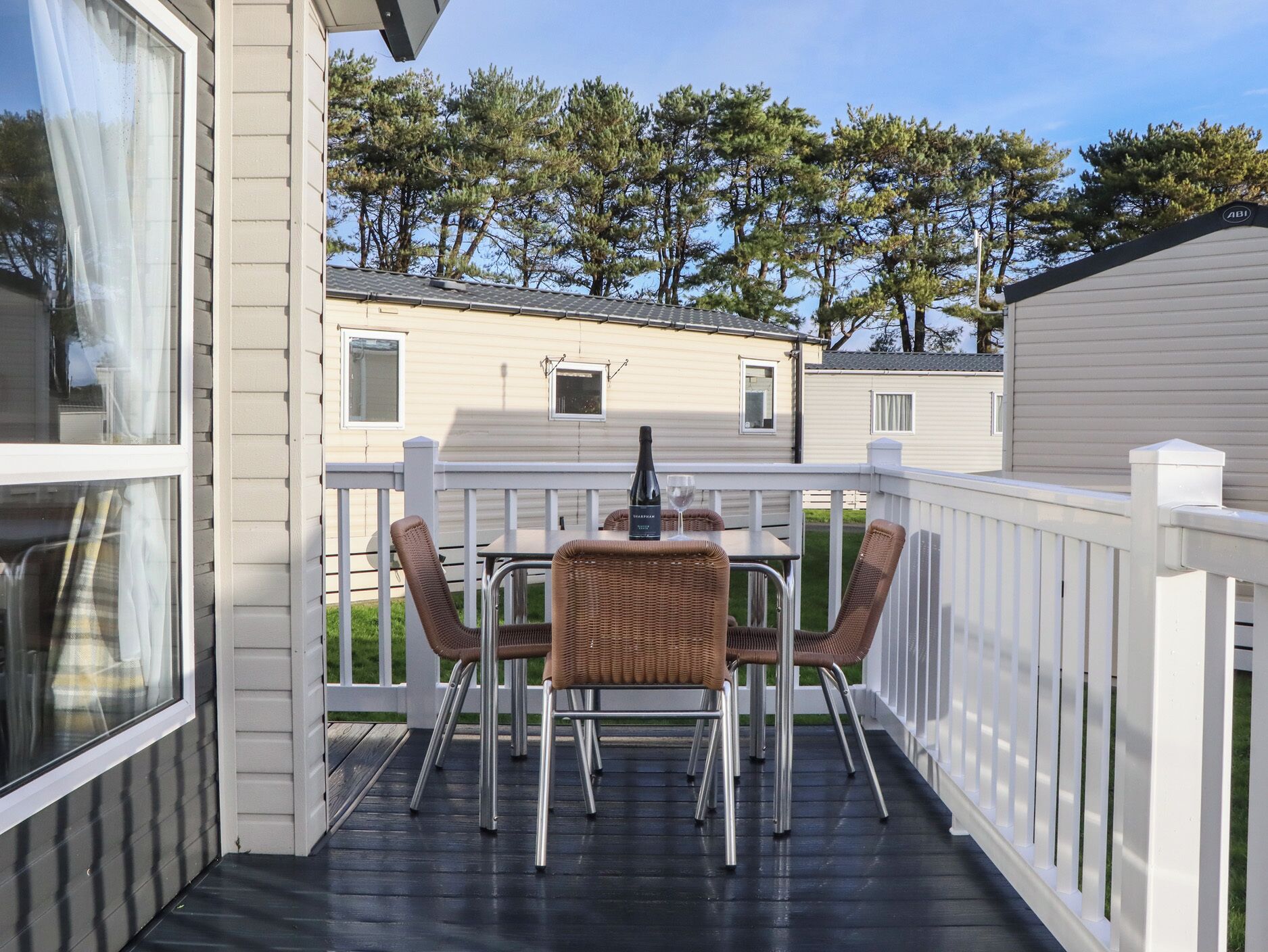 A covered outdoor patio with a table and four wicker chairs, a bottle of wine, and a glass on the table.