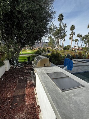 Ein Grill mit integriertem Abluftsystem, ein Poolbereich mit blauem Stuhl und im Hintergrund ein Blick auf einen Golfplatz.